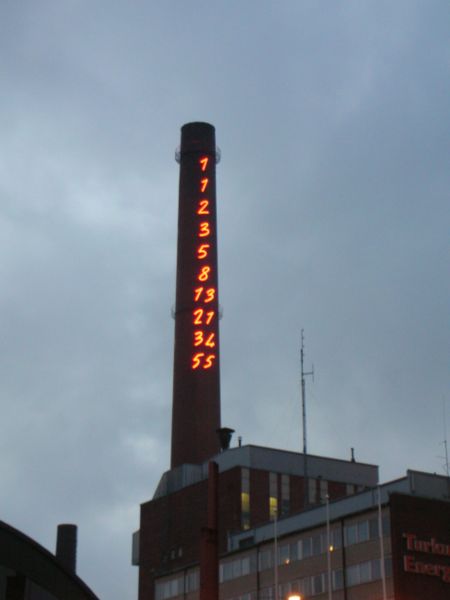 This photo shows the Fibonacci numbers 1, 1, 2, 3, 5, 8, 13, 21, 34 and 55 lit up on the side of a tall smoke stack. The Fibonacci sequence of numbers is named after the Italian mathematician Leonardo of Pisa (better known as Fibonacci). Born around 1170, Fibonacci is regarded as one of the greatest mathematicians of the Middle Ages.