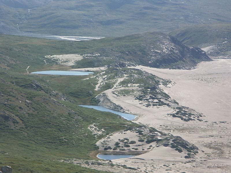 A high angled photo looking down on a large area of quicksand. Set amongst hilly sand dunes, this quicksand is a dangerous spot for those that don't read the warning signs.