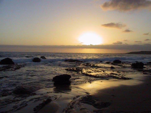 This photo shows a glorious sunset at the waters edge of a beautiful beach. The sun is fast dropping behind the clouds and beyond the horizon.