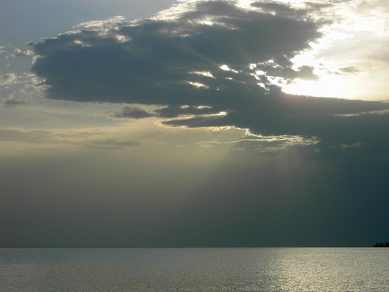 A spectacular photo of the sun trying to fight its way through some thick cloud at the end of a day full of sunshine and good weather. The suns rays are visible around the edges of the cloud as it manages to sneak its way through and reflect off the calm water below.